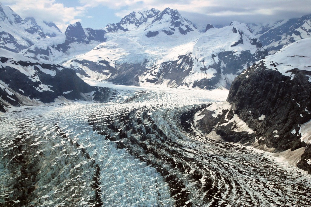 a rippled glacier cuts through snowy mountains