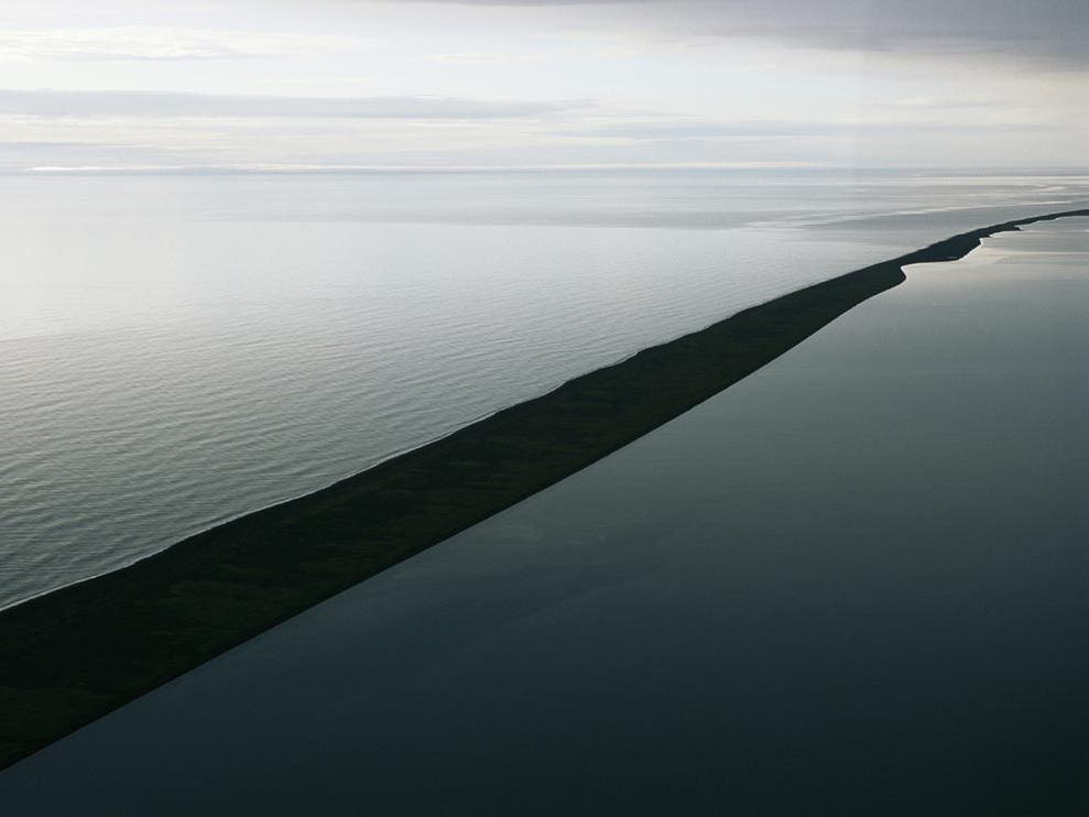 a sandbar off the Alaska coast separating one large body of water that spans to the horizon