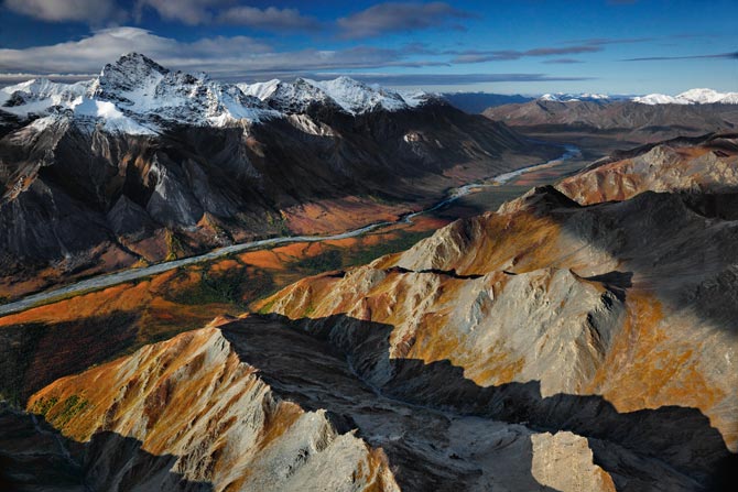 a river running between two mountains, one with a snow cap and the other with a rust or copper color