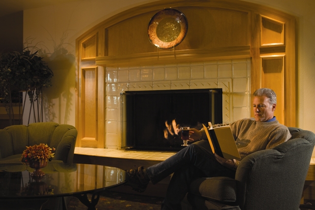 Man sipping coffee and reading book near the fireplace at Fairbanks Princess Riverside Lodge