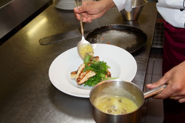 A chef spoons sauce over a dish.