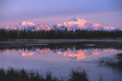 Sun setting on Alaska mountains with reflection on lake.