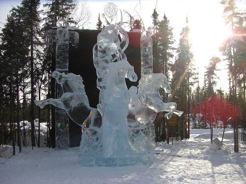 An ice sculpture glistening in the sunlight. Three ice carved horses are jumping out in each direction from the center of the sculpture. Fairbanks, AK