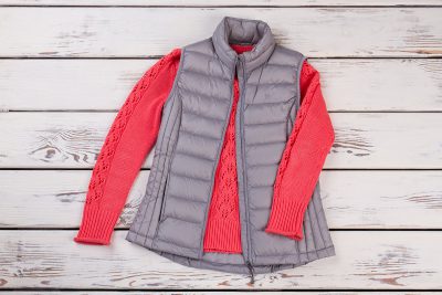 A puffy vest and sweater lay on a background of wood panels