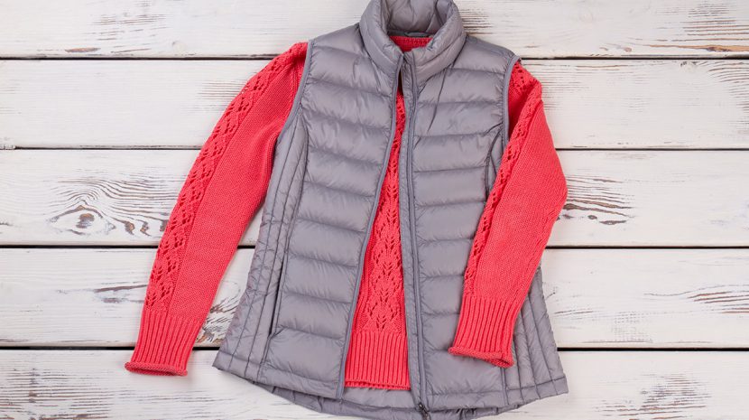 A puffy vest and sweater lay on a background of wood panels