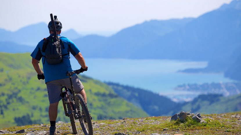 A cyclist pauses to take in the view of a lake at the base of mountains