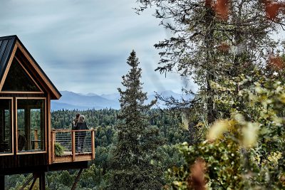 Two people stand on the deck of the treehouse at Mt McKinley Princess Wilderness Lodge